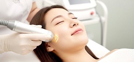 침대에 누운 여성의 얼굴에 핸드피스를 대고 시술을 진행하는 장면