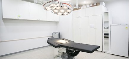 無影灯と施術ベッドが置かれた白い施術室の全景
