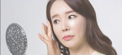 손거울을 들고 왼손으로 광대뼈 부위를 짚으며 피부를 살피는 여성